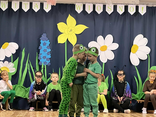 Zdjęcie przedstawia troje dzieci przebranych za zabki mówiących do mikrofonu na scenie