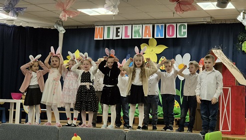 Zdjęcie przedstawia grupę przebranych w wielkanocne stroje dzieci, występującą na scenie