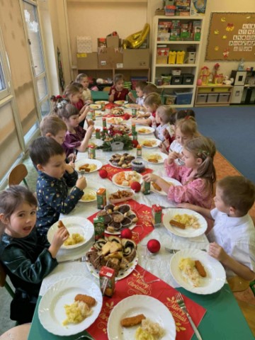 Na obrazku widać dzieci siedzące przy wigilijnym stole.