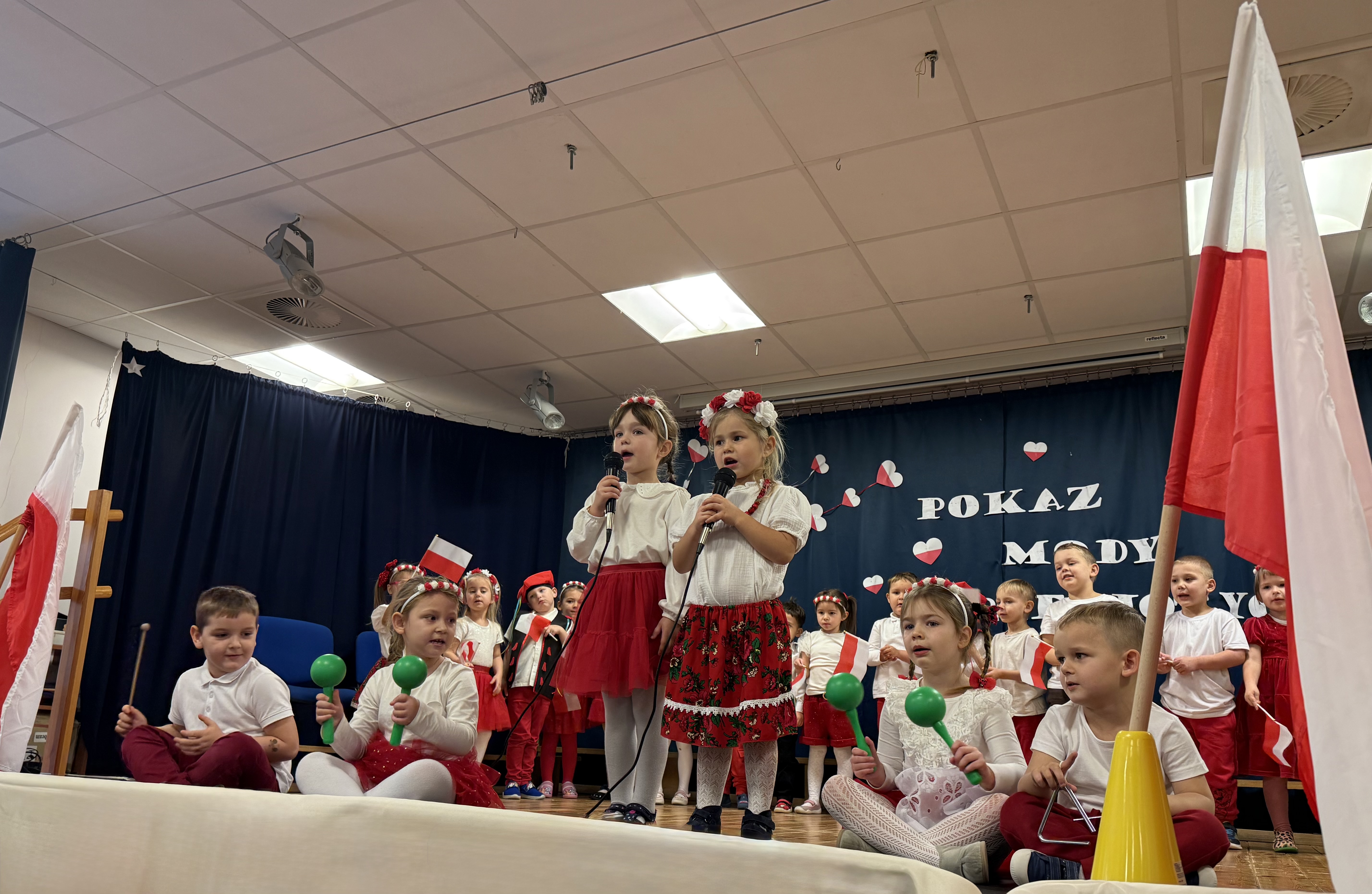 Zdjęcie przedstawia śpiewające dziewczynki, w tle grupa dzieci