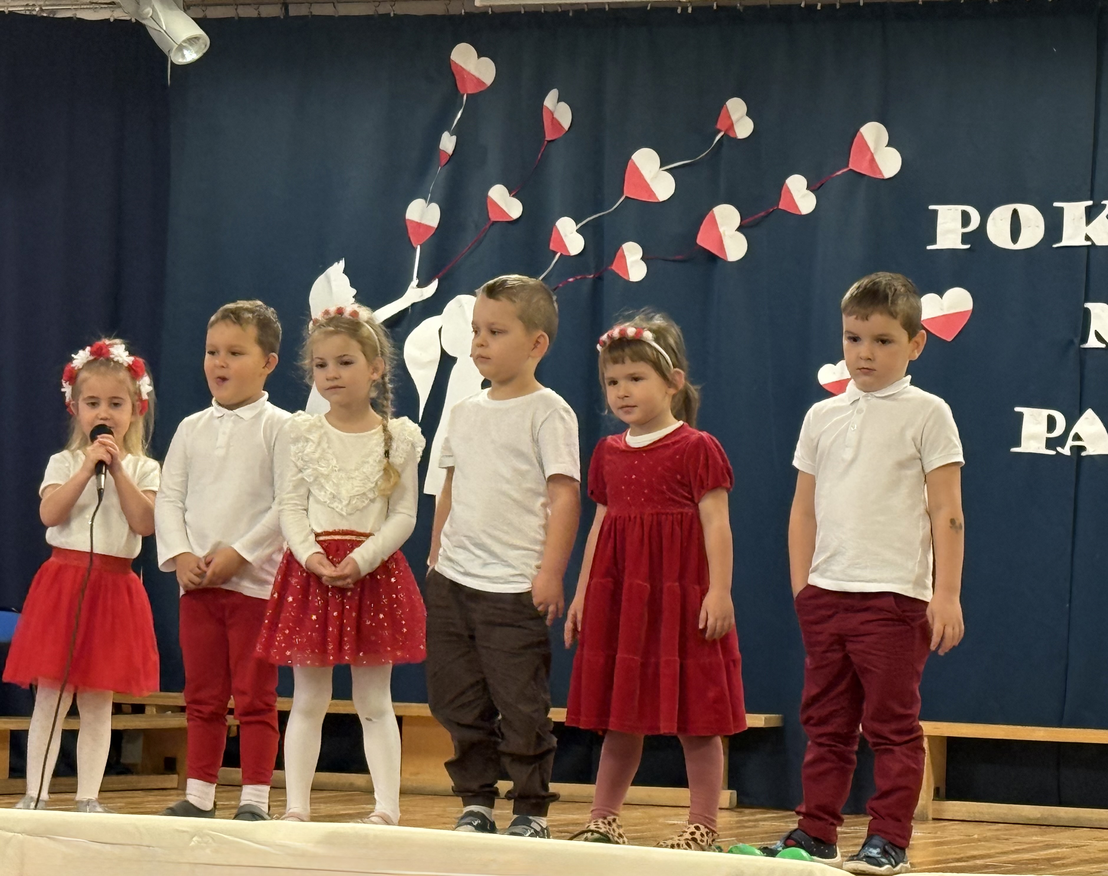 Zdjęcie przedstawia grupę dzieci na scenie podczas recytacji wiersza