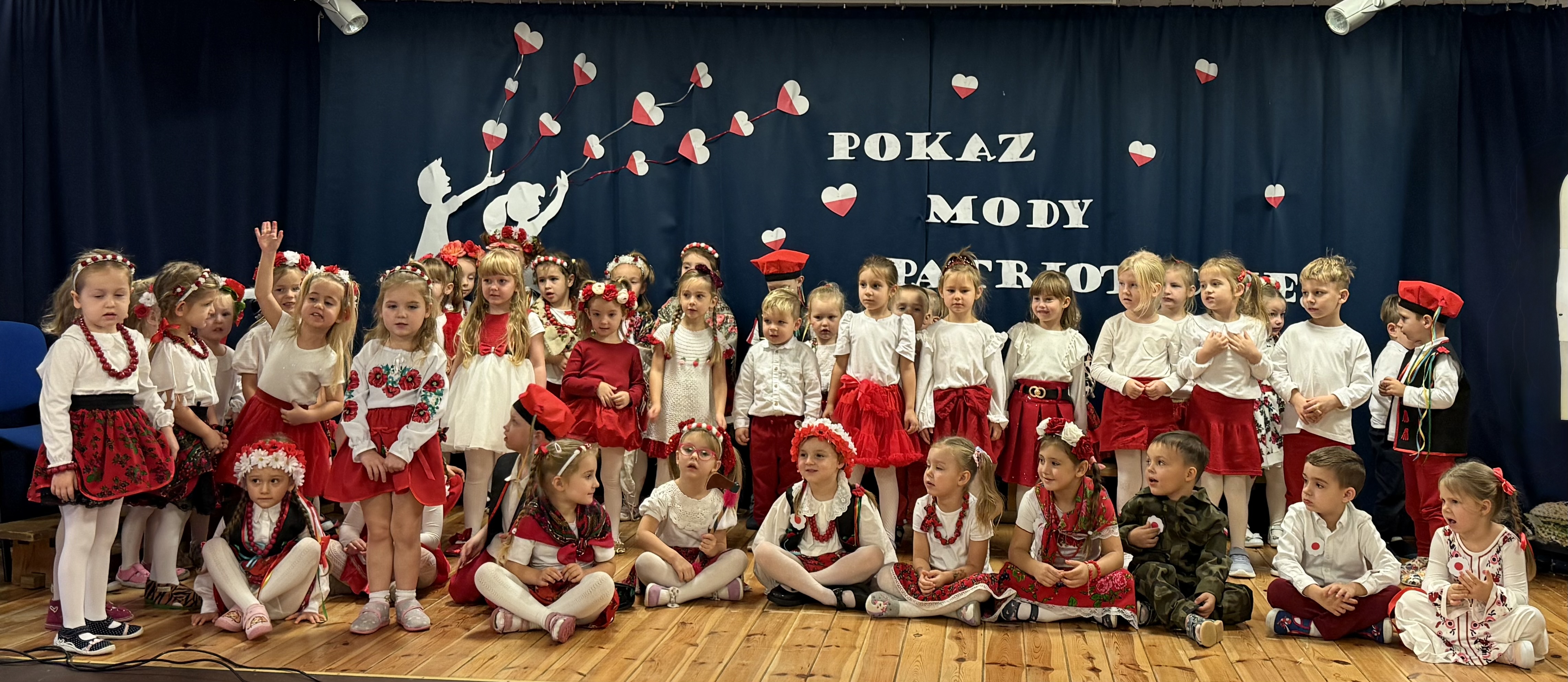 Zdjęcie przedstawia grupę dzieci ubraną w barwy narodowe na scenie