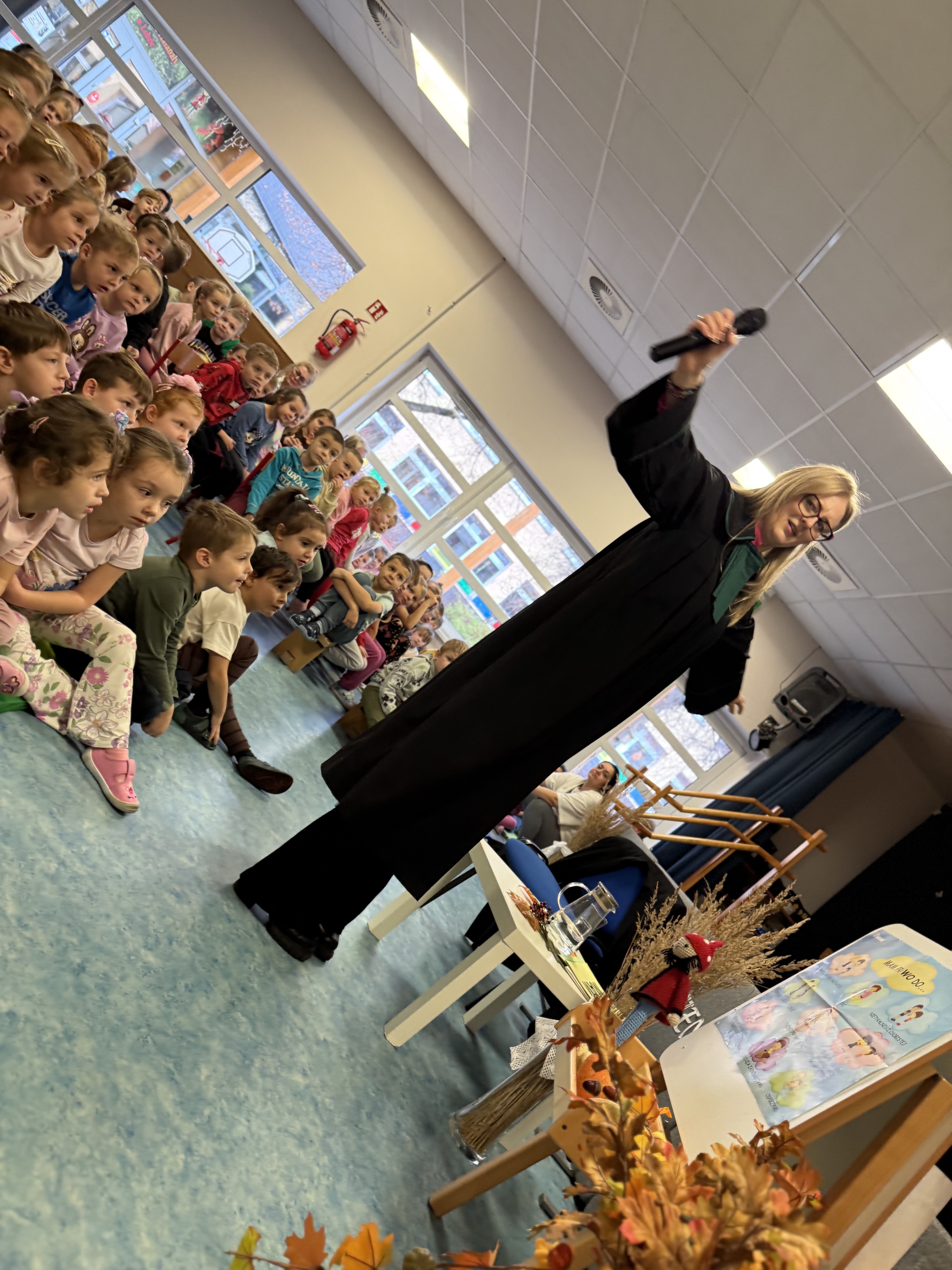 Zdjęcie przedstawia adwokat pokazującą dzieciom togę, w tle grupa dzieci