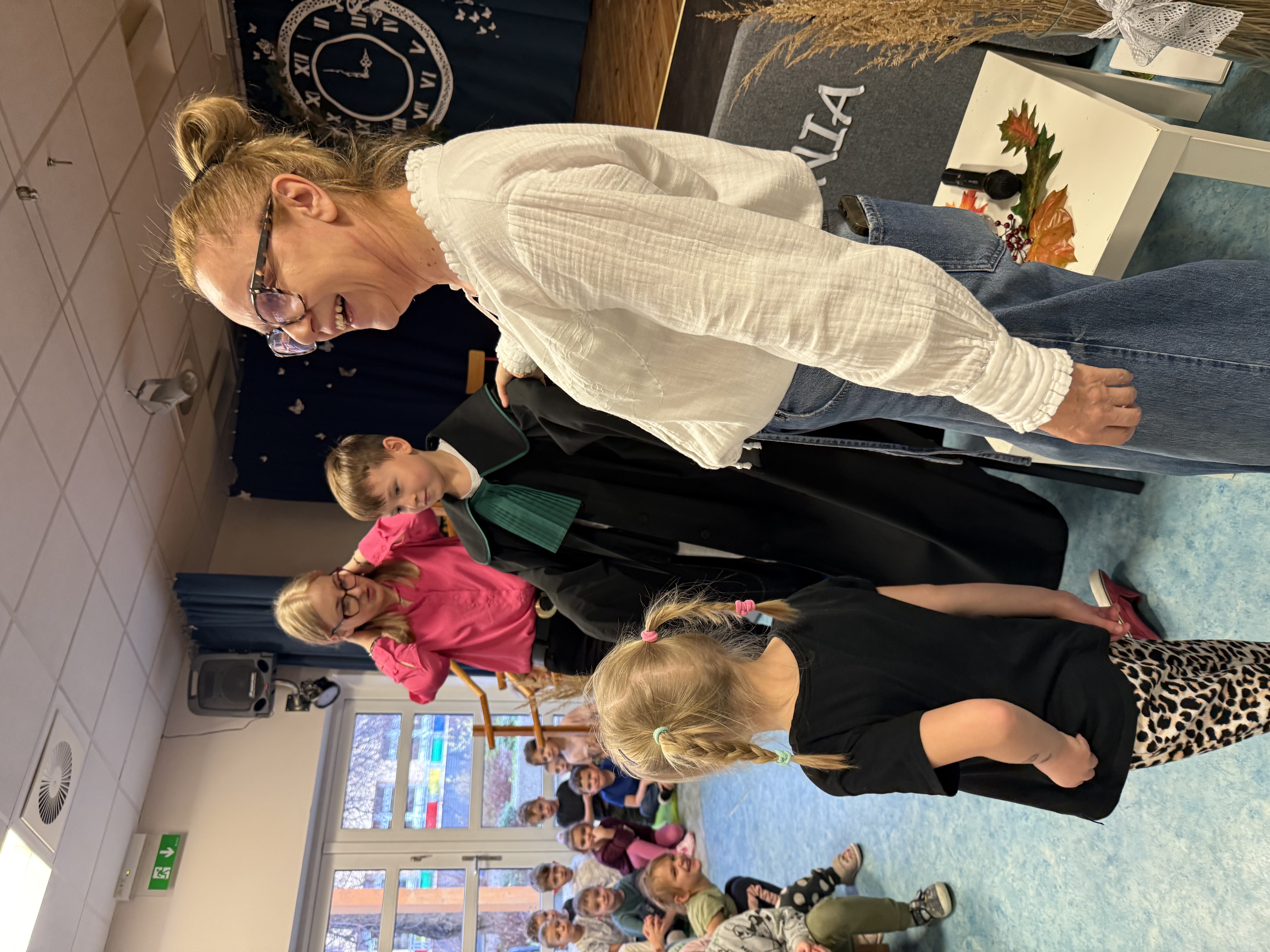 Zdjęcie przedstawia chłopca w todze adwokackiej oraz dwie kobiety, w tle grupa dzieci