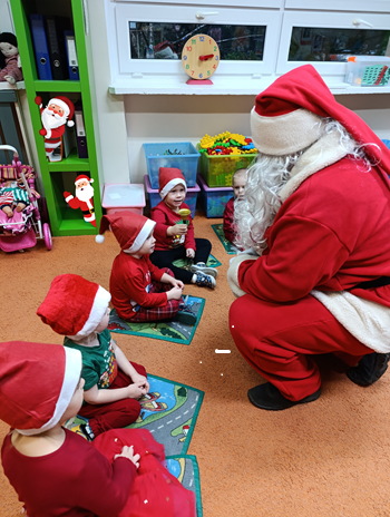 Na zdjęciu widzimy Mikołaja kucającego przy dzieciach siedzących na dywanie