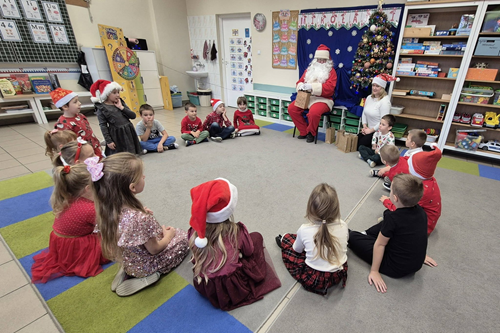 Na zdjęciu widzimy Mikołaja siedzącego w sali przedszkolnej, a przy nim w kole siedzące na dywanie dzieci