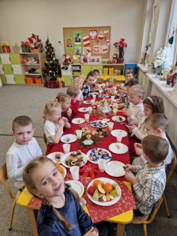 Na obrazku widać dzieci siedzące przy wigilijnym stole.